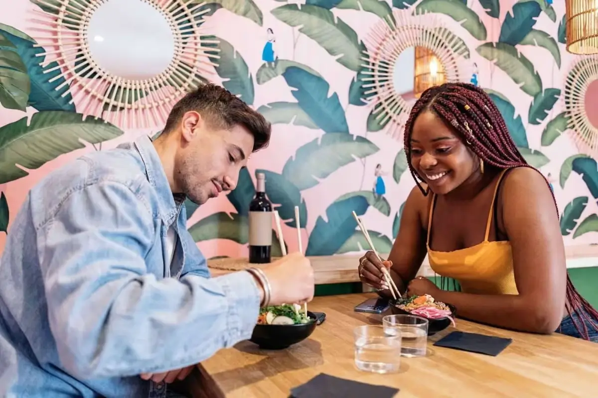 Couple enjoying a meal with chopsticks in a vibrant, tropical-themed restaurant.