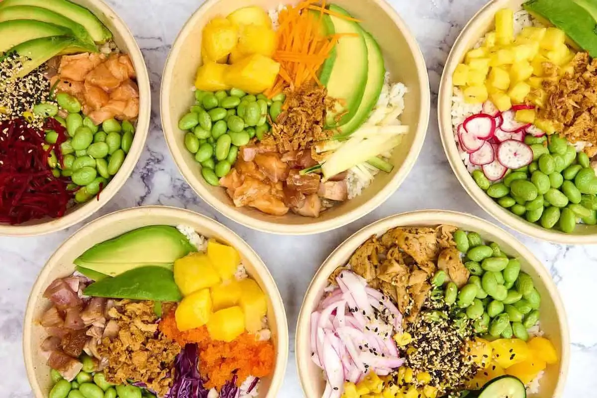 Five colorful poke bowls with fresh ingredients like avocado, edamame, mango, radish, and sesame seeds.