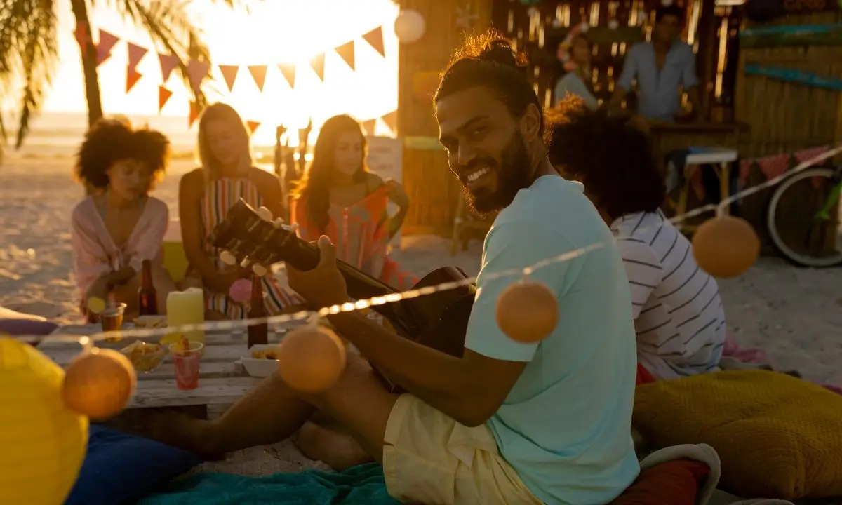 Summer beach party with friends enjoying music and catered poke bowls under warm sunset lighting.