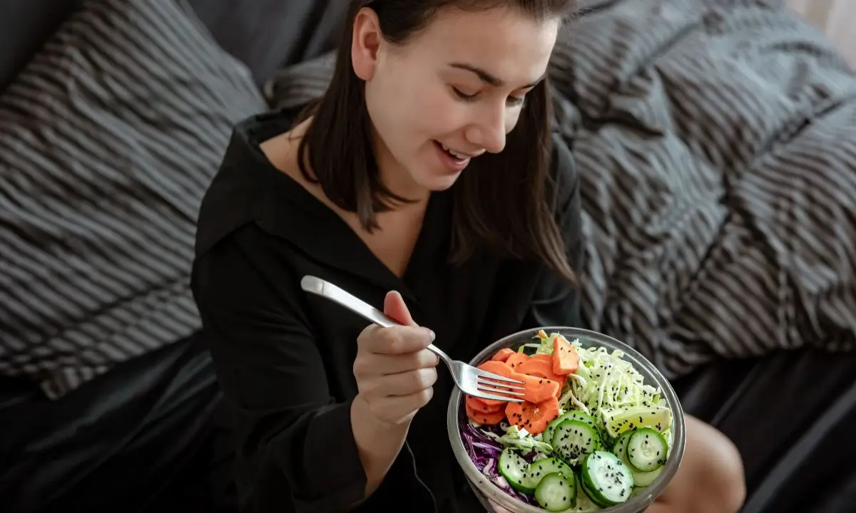 Woman enjoying homemade salmon poke bowl with fresh vegetables.