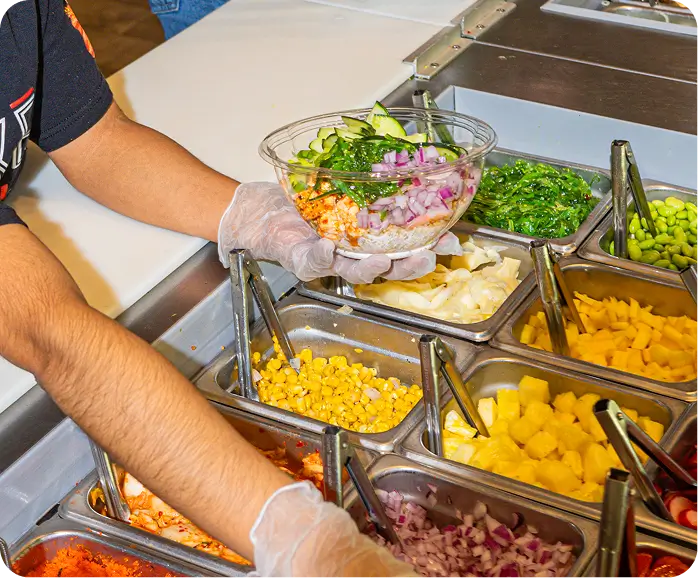 Gloved hands assembling a poke-style burrito bowl at Poke Bowl NY counter