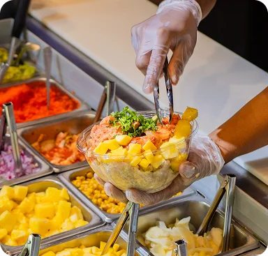 Gloved server assembling a bowl with diced mango, raw diced fish and cilantro